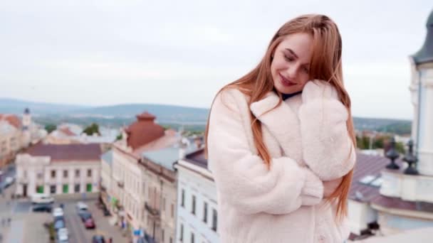 Ritratto di strada di giovane bella donna alla moda che indossa elegante giacca di eco pelliccia bianca passeggiando sul tetto della città vecchia. Modella che si guarda intorno. Street fashion concept . — Video Stock