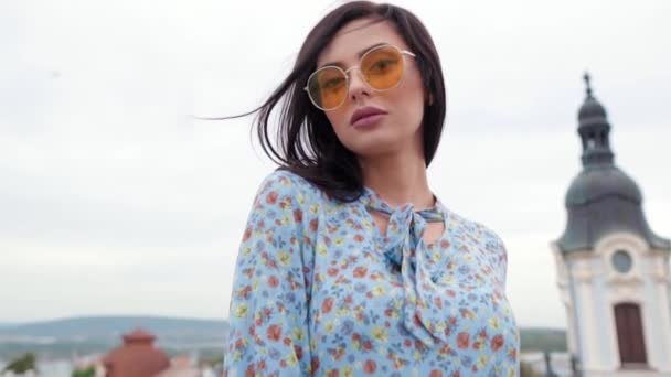 Young girl in blue dress and yellow sunglasses posing as a model for the photo shoot on the roof — Stock Video