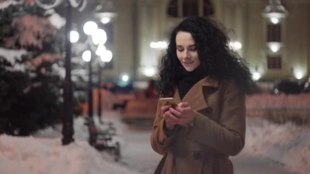 Woman Using Smart Phone at Night in the City. Attractive young woman texting, talking on smartphone outdoors. Blurred Night Busy Street lights background — Stock Video