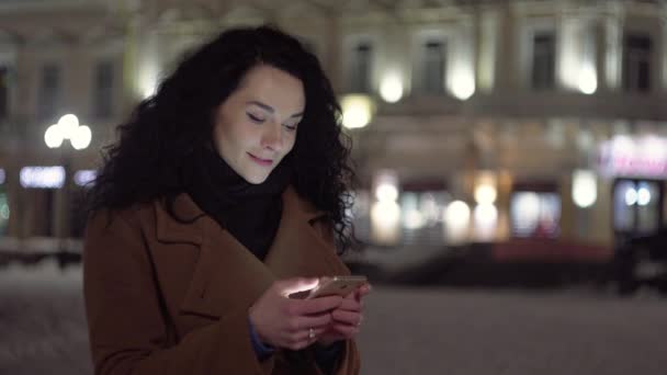 Attraktiv kvinna som använder mobiltelefon under promenaden på gatorna i Night Town — Stockvideo