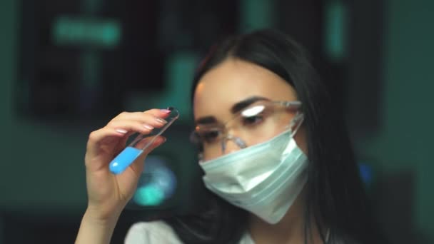 Une jeune scientifique examine une éprouvette contenant une substance rouge biologiquement dangereuse. Une fille dans des lunettes de protection et un masque examine une éprouvette rouge avec l'inscription dangereuse — Video