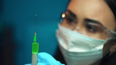 Professional female doctor in mask and gloves in hospital room with disposable one-off syringe with transparent drug. Woman physician at work. Laboratory employee making scientific research