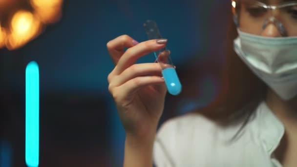 Eine medizinisch-wissenschaftliche Forscherin oder Ärztin, die in einem Labor ein Reagenzglas mit klarer Lösung betrachtet, im Vordergrund stehen Fläschchen. — Stockvideo