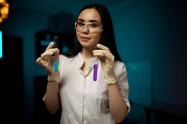Young chemical female researcher holding two glass tubes with fluid in laboratory