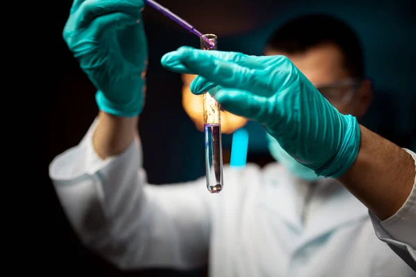 Tıp laboratuarındaki erkek bilim adamı test tüplerini pipetle dolduruyor. Kapat.