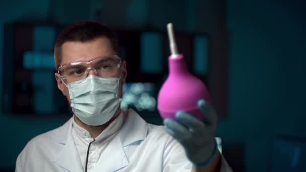 Médico masculino em uma máscara segura uma pêra médica em suas mãos e olha para a câmera — Vídeo de Stock