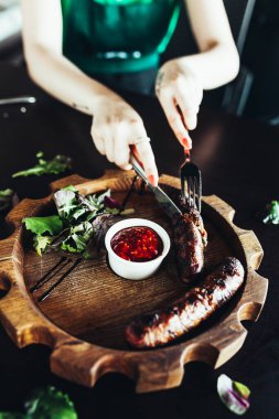 Kadınların elleri sosisi kesmek için çatal ve bıçak tutuyor. Bu soslu ızgara sosis.