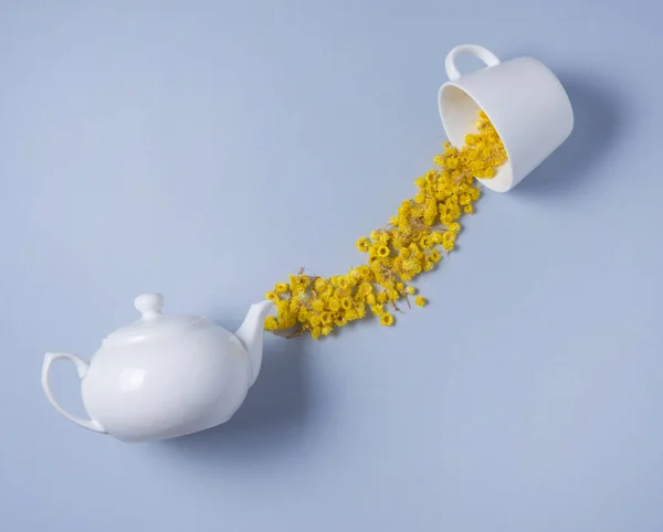 Kamillenblüten verschüttet aus einer weißen Teekanne in eine weiße Tasse — Stockfoto