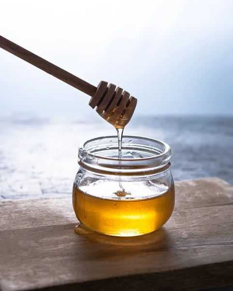Natural vegan golden honey in a jar on wood background. The hand holds a stick, which drains the honey. Image is macro, close up and front view