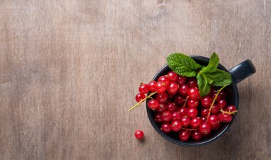 Kahverengi ahşap arka planda naneli taze kırmızı frenk üzümü.