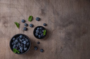 Kahverengi ahşap zemin üzerinde naneli iki kâse taze ve tatlı yaban mersini.