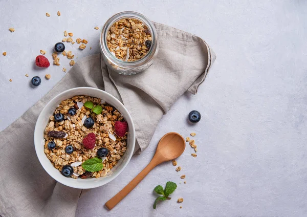 sweet granola with raspberry,  blueberry and coconut milk into white plate on light gray  table. Energy and vegan breakfast. Top view and copy space.