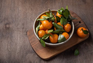 Tahta bir masada, bir kasede mini mandalinalar.