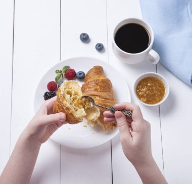 Elleri taze, glütensiz, ahududu, yabanmersini ve kumkuat reçelli kruvasan ve beyaz masa üzerinde bir fincan vegan taze demlenmiş kahve tutuyor. Sağlıklı ve diyet kahvaltı. Yukarıdan görünüşü