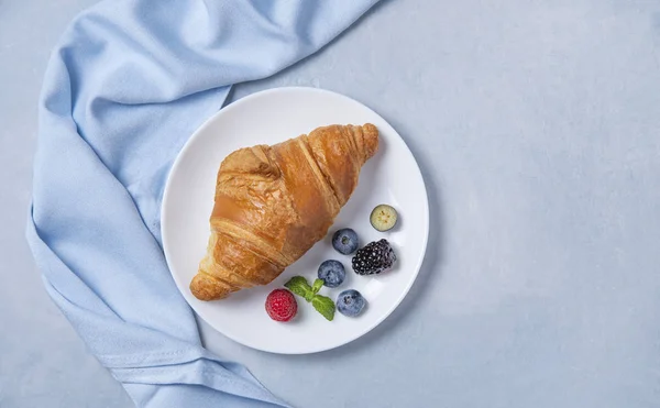Fresh  croissant on a white plate and a blue napkin with berries — 스톡 사진