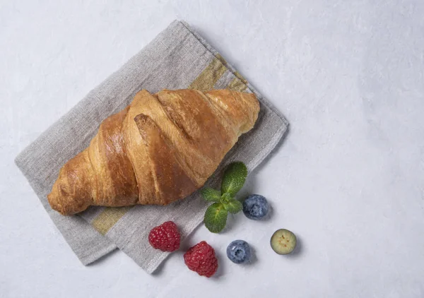 Fresh  croissant on a grey napkin with berries on a grey background — 스톡 사진