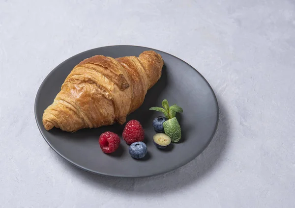 Fresh  croissant on a   grey plate with berries on a grey background — 스톡 사진