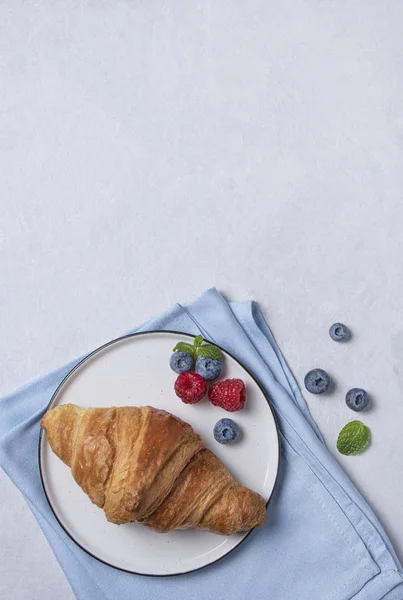 Świeży rogalik na białym talerzu i niebieska serwetka z jagodami — Zdjęcie stockowe