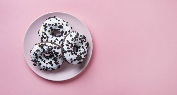 three delicious fresh hearty black and white donuts lie on a pink background