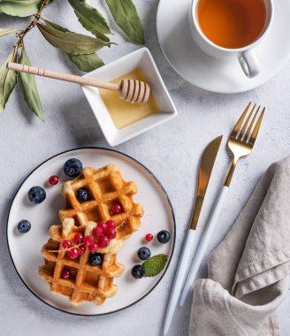Böğürtlenli taze Belçika waffleları ve kırmızı frenk üzümü, bal ve çay beyaz bir masada. Nefis bir kahvaltı. Üst görünüm ve düz uzanma