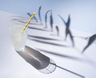 Gri mavi arka planda, palmiye dallarının sert gölgeleriyle bir bardak taze limonata.