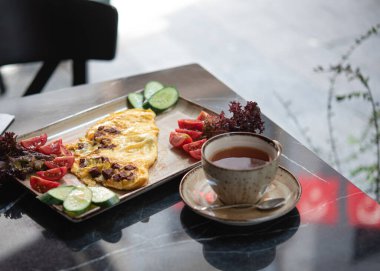 Kafede yaz kahvaltısı. Taze sebzeli sahanda yumurta ve siyah mermer bir masada çay.