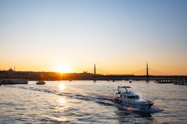 Yazın İstanbul 'da gün batımında güneşli bir manzara. Mavi camiyi gören Boğaz 'ı geçerek. Köprünün altından turistlerle dolu bir gemi geçiyor