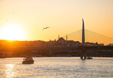 Yazın İstanbul 'da gün batımında güneşli bir manzara. Mavi camiyi gören Boğaz 'ı geçerek. Köprünün altından turistlerle dolu bir gemi geçiyor