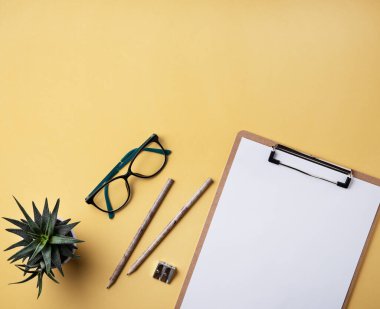 Ev ödevi. Not, kalem, gözlük ve sarı arka planda sulu bir iş yeri. Resim üst görünümü, düz görünüm ve boşluk kopyala