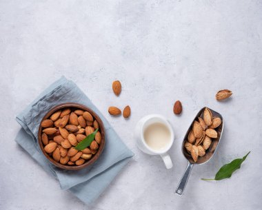 Tahta bir kasede badem, mavi bir peçetede badem sütü ve gri arka planda çiğ fındık. Üst görünüm ve kopyalama alanı