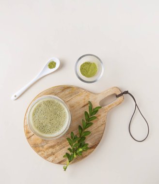 Tahtanın üzerinde açık bir bardakta taze kibrit çayı ve sarı arka planda beyaz kaşık. Moda içeceği. Üst görünüm, düz görünüm ve boşluk kopyala