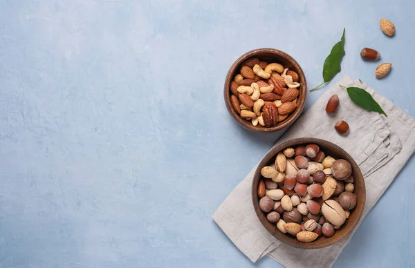 a mixture of nuts in two wooden bowls on gray napkin on a blue background. Vegan product. Top view and copy space