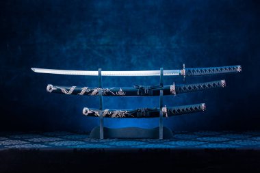 Kürsüde üç kılıç, katana bıçağı açıkta, arkasında mavi ışık