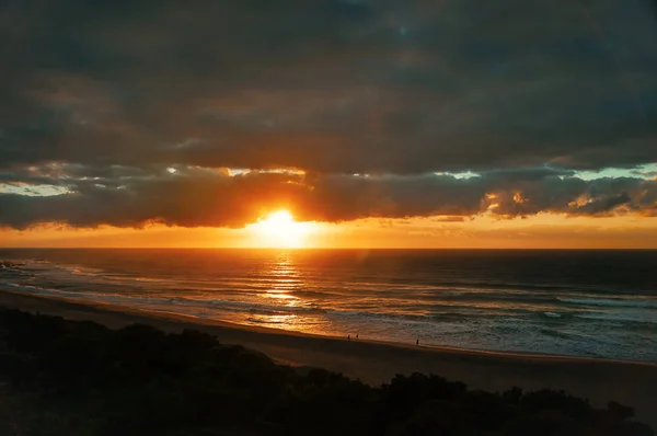 Früher Sonnenaufgang am Meeresstrand, mit Silhouetten von spazierenden Menschen — Stockfoto