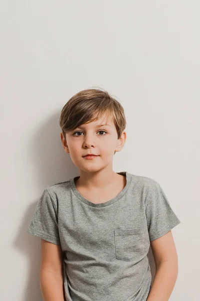 Ładny chłopak stojący obok biała ściana, szara koszula, uśmiechając się — Zdjęcie stockowe