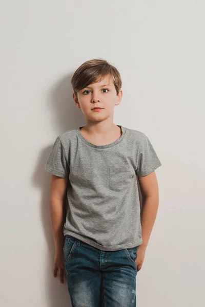 Chłopiec z scared twarzy biała ściana, szara koszula, dżinsy — Zdjęcie stockowe