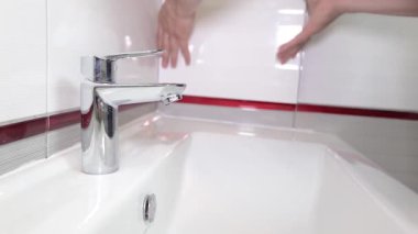 İşçi elleri yeni bitmiş bir banyoda musluğu açıyor. Lavabonun yanındaki beyaz seramik duvara monte edilmiş su sistemini gösteriyor. Modern tasarım, minimalizm kavramı