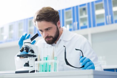 Kimya laboratuarı. Arka planda çalışan yakışıklı bir profesyonel kimyager ile masada duran test tüpleri ise seçici odak