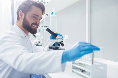 Biyolojik araştırma. Pozitif akıllı erkek biyolog bir mikroskop tutan ve biyolojik bir araştırma yaparken bir test tüpü alarak