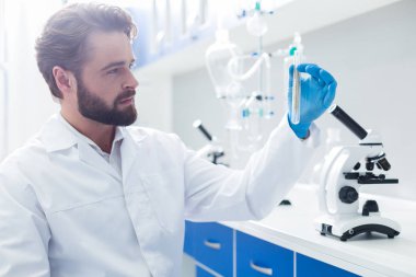 Biyolojik araştırma. Pozitif akıllı erkek biyolog bir mikroskop tutan ve biyolojik bir araştırma yaparken bir test tüpü alarak