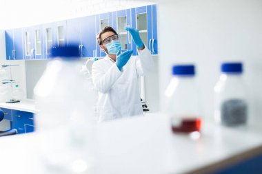 Biyo laboratuvar. Akıllı güzel yakışıklı bilim adamı laboratuvarda ayakta ve biyolojik bir araştırma yaparken test tüpü bakarak