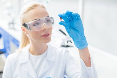 Yenilikçi tedavi. Laboratuvarda çalışırken neşeli bir pozitif kadın bilim adamı tarafından tutulan yeni bir ilacın seçici odak