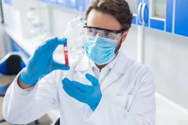 DNA araştırması. Nice profesyonel erkek doktor bir kan örneği tutan ve tıbbi laboratuvarda çalışırken ona bakarak