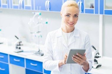 Dijital alet. Nice memnun olumlu kadın bir tablet kullanarak ve modern laboratuvarda çalışırken gülümseyerek