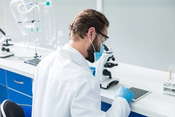 Modern Technology Nice Serious Professional Scientist Sitting Table Wearing Mask — Stock Photo, Image