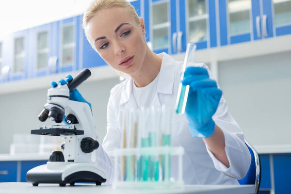 Medical lab. Smart intelligent nice woman holding a test tube and looking at it while working in the lab