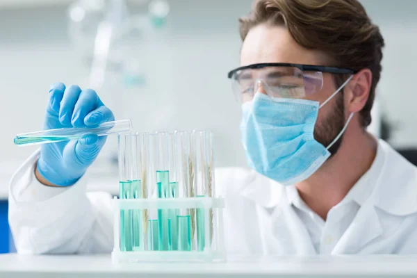 有機化学素敵なスマートな男性化学者によって見られている間 シェルに立っている試験管の選択的な焦点 — ストック写真
