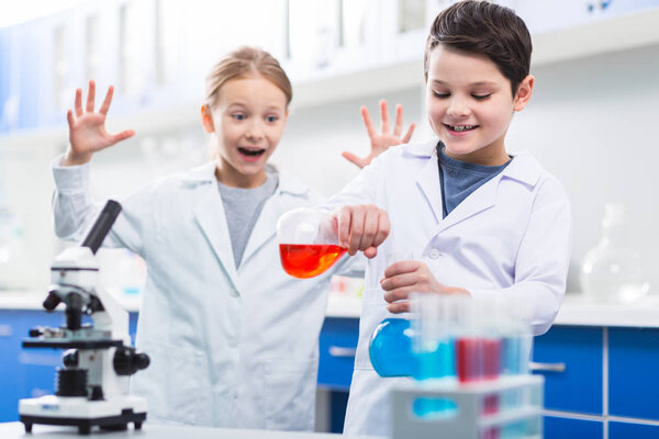 Not do it. Good looking glad boy mixing liquids while frightened girl shouting and standing behind him