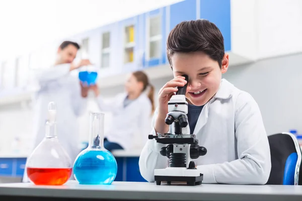 Alegre chico alegre mirando a través del microscopio — Foto de Stock