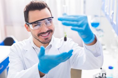 Bilimsel bir buluş. Neşeli gay erkek laboratorian şişe bitki yetiştirirken güvenlik cam giyen ve gülümseyen